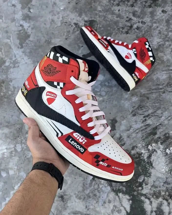 Red, white, and black high-top sneakers with various brand logos on a concrete floor.